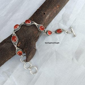 May include: A silver bracelet with a toggle clasp and red carnelian stones. SterlingSilverRing92.