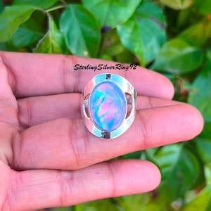 May include: A silver ring with a large oval-shaped iridescent gemstone set in a silver bezel. The gemstone has shades of blue, pink, and purple.