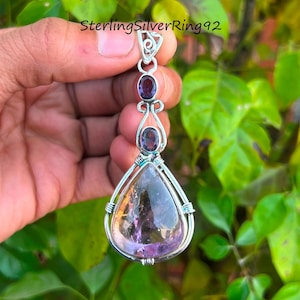 May include: A teardrop-shaped pendant with a large amethyst gemstone set in silver wire. The pendant has two smaller amethyst gemstones above the large one, and a silver bail at the top.