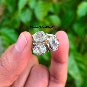 May include: A silver ring featuring three clear, faceted stones. The stones are set in a band crafted from sterling silver. The ring is worn on a finger.