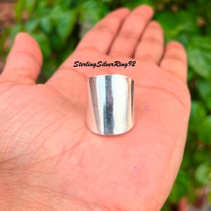 Peut inclure: Une bague en argent avec une large bande plate. La bague est lisse et brillante.