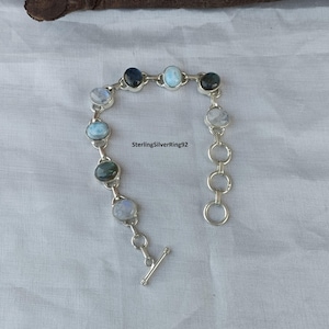 May include: A silver bracelet with a toggle clasp features a chain with alternating blue and white oval gemstones. The bracelet is on a white surface.