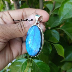 May include: A silver pendant with a large oval blue labradorite gemstone. The pendant has a silver bail for attaching to a chain.