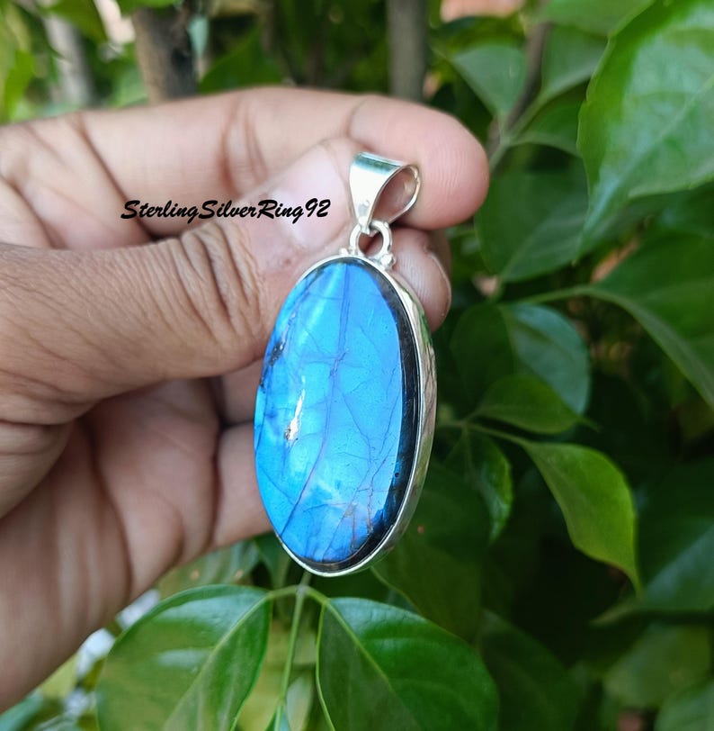 May include: A silver pendant with a large oval blue labradorite gemstone. The pendant has a silver bail for attaching to a chain.