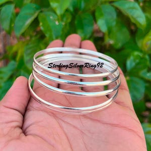 May include: Set of five silver bangles stacked on top of each other. The bangles are smooth and shiny.