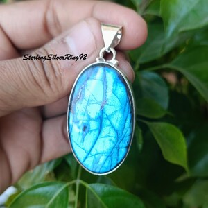 May include: A silver pendant with a large oval-shaped blue labradorite gemstone. The stone has a shimmering iridescent effect.