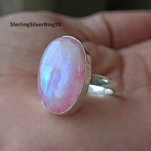 Könnte beinhalten: Ein Silberring mit einem großen ovalen Mondstein. Der Mondstein ist hellrosa mit einem blauen, schillernden Schimmer.