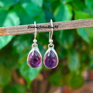 May include: Sterling silver earrings with teardrop-shaped amethyst gemstones. The earrings are a light purple color and have a shiny finish.
