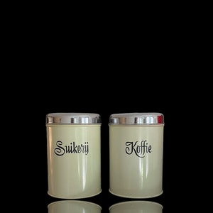 May include: Two vintage metal canisters with silver lids. The canister on the left says "Suikerij" and the canister on the right says "Koffie".