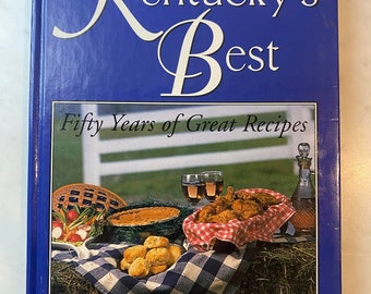 Könnte beinhalten: Ein blaues Buch mit dem Titel "Kentucky's Best: Fifty Years of Great Recipes" von Linda Allison-Lewis. Der Umschlag zeigt ein Foto einer karierten Tischdecke mit einem Korb frittierten Hühnchens, einem Kuchen, einer Auflaufform und zwei Gläsern Wein.
