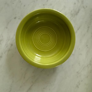 May include: A top-down view of a chartreuse-colored bowl with concentric circles in the center. The bowl is made of ceramic and sits on a white marble surface. The bowl's design is simple and classic, suitable for serving food.