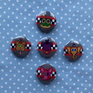 May include: Five round buttons with black and white chequered borders. Each button features a different cartoon character with a red, white and black colour scheme. The characters include a frog, a fox, a purple creature with a top hat, an elephant and a pig.