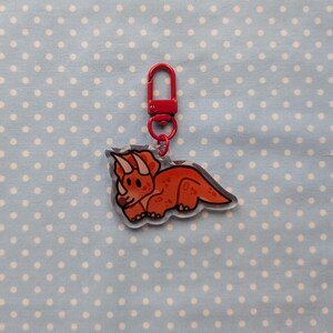 May include: A red and white cartoon triceratops keychain with a red metal key ring.