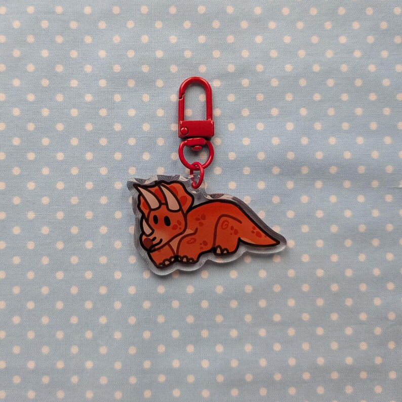 May include: A red and white cartoon triceratops keychain with a red metal key ring.