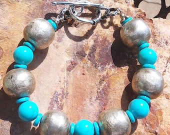 May include: A silver and turquoise bracelet with a toggle clasp. The bracelet features large, round silver beads and smaller turquoise beads.