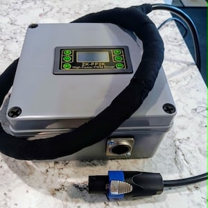 May include: A gray electronic device with the text "ZK-PP2K High Power PWM Driver" on the front. It has a black cable wrapped around it and a black and blue connector. The device has a small screen and several buttons.
