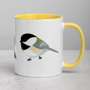 May include: White ceramic mug with a yellow rim and handle. The mug features a hand-painted illustration of a black-capped chickadee bird.
