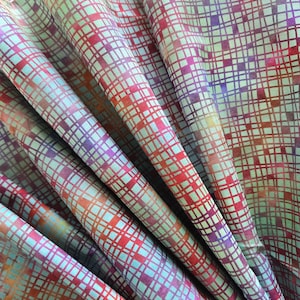 May include: Close-up of colourful fabric with a grid pattern. The fabric features a repeating pattern of squares in shades of red, purple, orange, and blue. The fabric is folded, creating a layered effect.