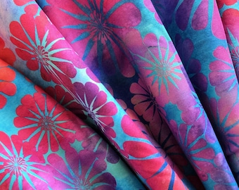 Op de afbeelding: Close-up van een levendige stof met een bloemenpatroon. Het ontwerp toont grote, gestileerde bloemen in tinten rood, roze en turquoise tegen een donkerblauwe achtergrond. De stof is gevouwen en toont het herhalende patroon.