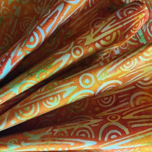 May include: Orange fabric with a white and green batik pattern. The fabric is folded and shows the pattern on both sides.