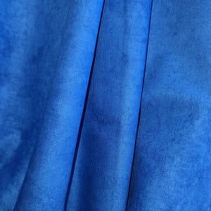 Può includere: Primo piano di un tessuto blu vibrante con una trama sottile e pieghe. Il colore del tessuto è un blu ricco e saturo, con variazioni di tono che creano profondità. Le pieghe aggiungono dimensione e interesse visivo al tessuto.