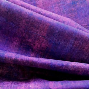 May include: Close-up of a fabric with a textured, abstract design. The fabric features shades of purple and blue, with a mottled appearance. The folds and shadows create depth and visual interest. The overall theme is artistic and textile-focused.
