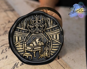 May include: A black wax seal with a gold design of a grand piano, a violin, and a chandelier. The seal is on a piece of old paper with writing.