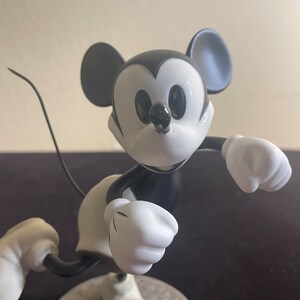May include: Black and white figurine of Mickey Mouse running with his arms outstretched. The figurine is made of ceramic and has a glossy finish.