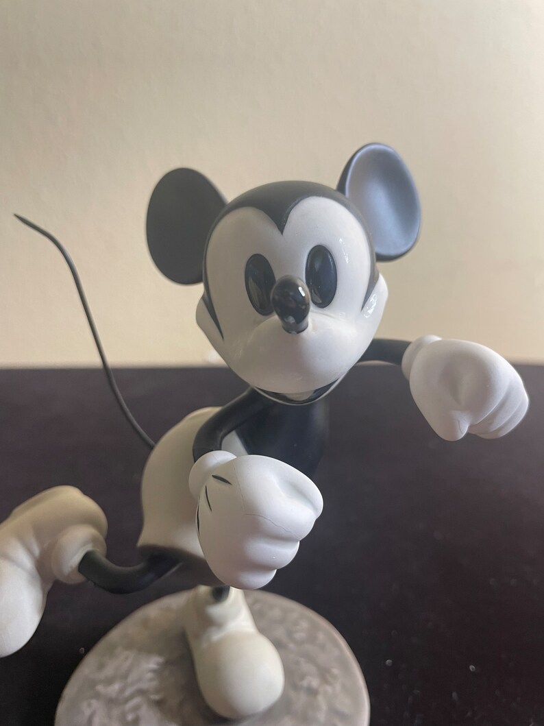 May include: Black and white figurine of Mickey Mouse running with his arms outstretched. The figurine is made of ceramic and has a glossy finish.