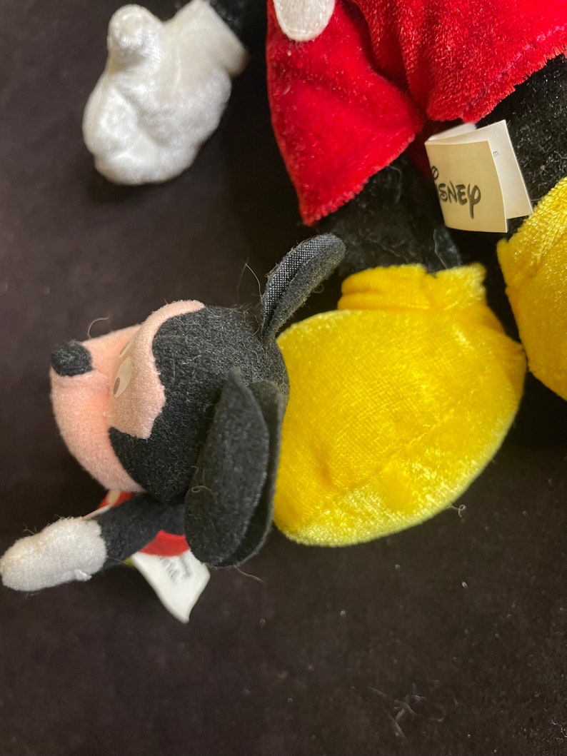 K&ouml;nnte beinhalten: Nahaufnahme eines Pl&uuml;schtier-Sets mit Mickey Mouse und Pluto. Mickey tr&auml;gt seine charakteristischen roten Shorts und gelben Schuhe. Pluto tr&auml;gt ein rotes Halsband. Die Spielzeuge haben ein Disney-Etikett.