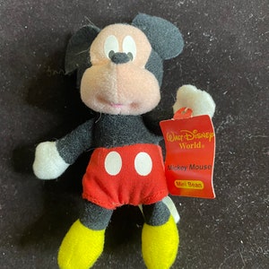 K&ouml;nnte beinhalten: Ein kleines schwarzes und rotes Pl&uuml;schtier Mickey Mouse mit gelben Schuhen. Das Spielzeug ist mit "Walt Disney World" und "Mickey Mouse Mini Bean" beschriftet.