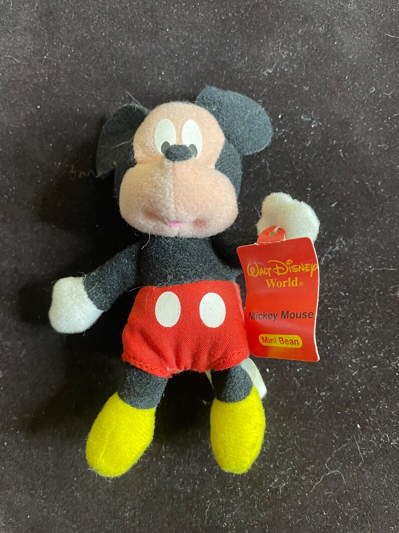 K&ouml;nnte beinhalten: Ein kleines schwarzes und rotes Pl&uuml;schtier Mickey Mouse mit gelben Schuhen. Das Spielzeug ist mit "Walt Disney World" und "Mickey Mouse Mini Bean" beschriftet.