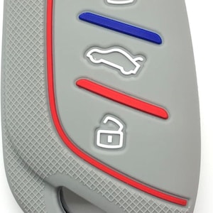 Puede incluir: Funda gris para mando de llave de coche con detalles en rojo y azul. La funda tiene una superficie texturizada y presenta iconos blancos para bloquear, desbloquear y abrir el maletero. El diseño incluye un borde rojo.