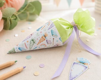 May include: A cone-shaped school gift bag featuring a pattern of books, pencils, and rainbows, topped with light green tissue paper and tied with a lavender ribbon. A matching cone-shaped gift tag lies nearby, alongside two wooden pencils.