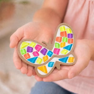 May include: A butterfly-shaped craft piece featuring a brown wooden frame filled with a mosaic of small, colorful glass tiles in shades of neon yellow, bright orange, purple, hot pink, light blue, and lime green set against a white base.