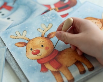 May include: A festive felt square featuring a reindeer illustration with a red scarf and nose, set against a light blue snowy backdrop. Other squares with Santa and snowman illustrations are visible. A hand is holding a wooden tool.