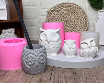 May include: Four white owl-shaped ceramic candle holders, two small and two large, on a gray circular tray. The larger owls are on a pink surface. The smaller owls are on a white surface.