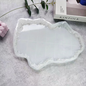 Op de afbeelding: Een transparante, witte siliconen mal in de vorm van een onregelmatige, organische vorm met een glad, vlak interieur. De mal is ontworpen voor het gieten van hars en heeft een getextureerde, verhoogde rand.