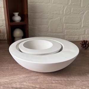 Può includere: Due ciotole in ceramica bianca, una annidata nell'altra. Le ciotole sono rotonde e hanno una finitura liscia e opaca.