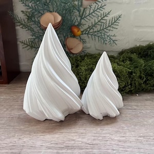 May include: Two white ceramic Christmas trees with a swirl design. The larger tree is on the left and the smaller tree is on the right.