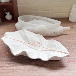 Könnte beinhalten: Zwei weiße Silikonformen zum Herstellen von Blattformen. Die größere Form ist 27 cm lang und 14 cm breit. Die kleinere Form wiegt 278 Gramm.