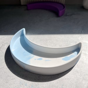 Peut inclure: Un plat en forme de croissant de lune blanc et bleu clair. Le plat est en céramique et présente un motif marbré.