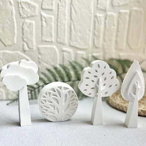 Könnte beinhalten: Set aus vier weißen Keramik-Baumschmuck mit verschiedenen Designs. Die Bäume sind alle unterschiedlich hoch und haben einen einfachen, modernen Stil.