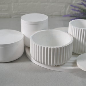 May include: Four white ceramic containers with lids. Two of the containers have a ribbed design. The containers are arranged on a white surface.