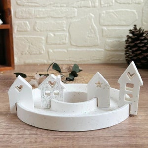 May include: White ceramic house-shaped candle holders arranged in a circle on a white speckled ceramic base. The houses have heart and star cutouts.