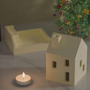 Może przedstawiać: Kremowy ceramiczny świecznik w kształcie domu z prostokątnymi oknami i kominem. Obok znajduje się pasująca prostokątna taca ze schodami. Przed domem stoi zapalona świeczka typu tea light. W tle choinka.