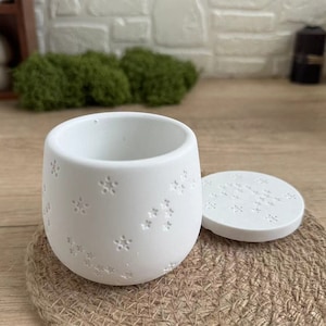 May include: White ceramic container with a lid, both decorated with a small white star pattern. The container is sitting on a woven brown surface.