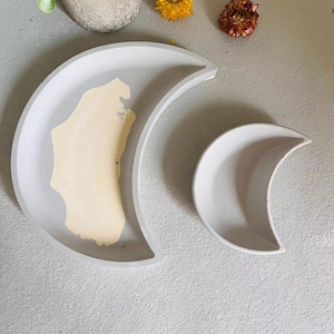 Op de afbeelding: Twee grijze halve maanvormige schalen. De grotere schaal heeft een lichtgele binnenkant. De kleinere schaal is effen grijs.