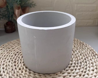 May include: A plain white cylindrical concrete planter pot, sitting on a woven wicker coaster.