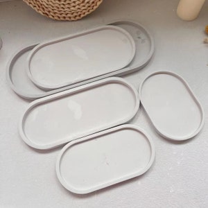 May include: Four oval-shaped, light gray, concrete trays of varying sizes. The trays are arranged in a staggered pattern on a white surface.